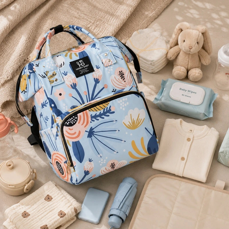 Sac à dos à langer bébé bleu fleuri entouré d'accessoires de puériculture