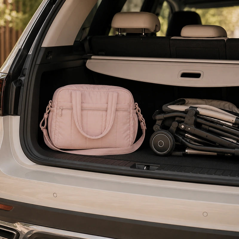 Sac à langer épaule rose posé dans le coffre d'une voiture à côté d'une poussette pliée
