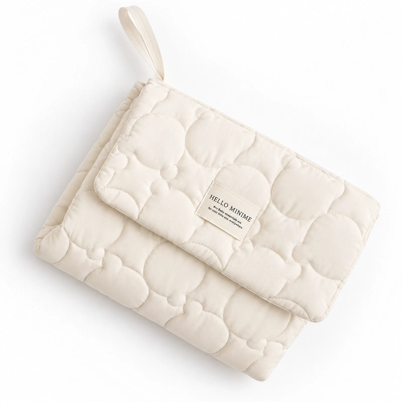 Tapis de change bébé matelassé écru plié avec poignée de transport, format compact nomade