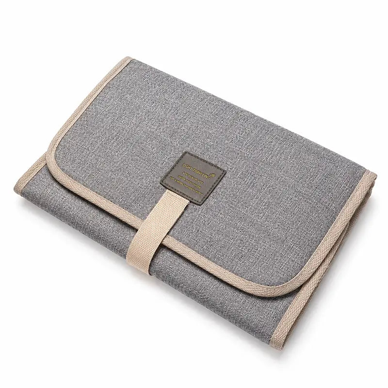 Tapis de change bébé nomade plié gris clair avec sangle de fermeture, format compact voyage